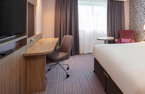 a hotel room with a bed, chair, desk and television at Leonardo London Heathrow Airport in Hillingdon