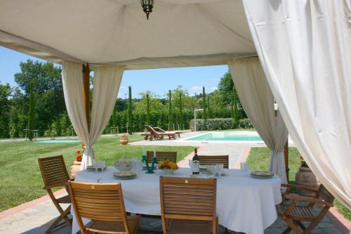 un tavolo da pranzo sotto una tenda con piscina di Villa Cappuccini a Castiglion Fiorentino