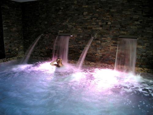 a woman sitting in a pool in front of a waterfall at Hotel Rural y SPA Kinedomus Bienestar in Aranda de Duero