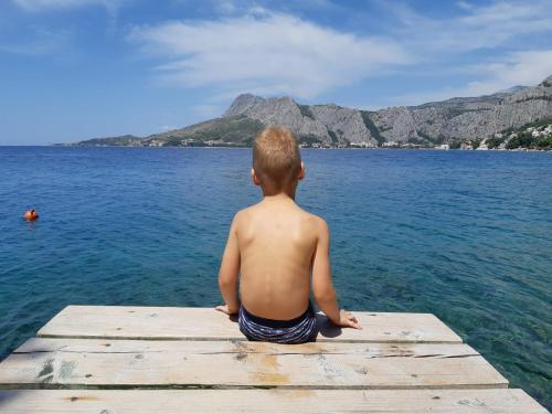a young child sitting on a dock looking out over the water at Cozy apartments with seafront terraces in Omiš