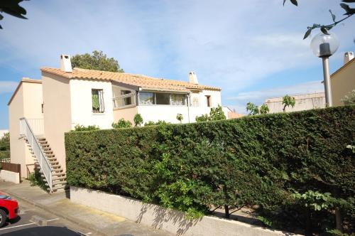 a white house with a hedge in front of it at Appartement La Pinède in Gruissan