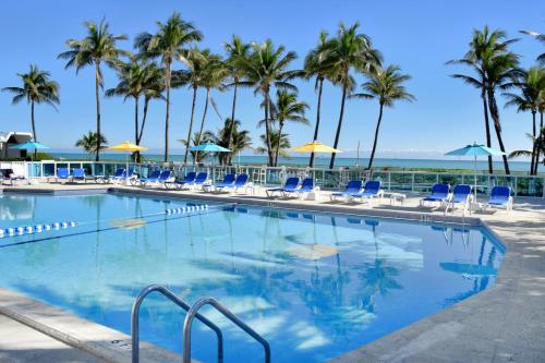 a swimming pool with chairs and palm trees at Seacoast Suites on Miami Beach in Miami Beach