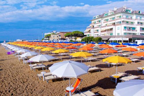 un mucchio di ombrelloni e sedie su una spiaggia di Pensione Imperia a Lignano Sabbiadoro