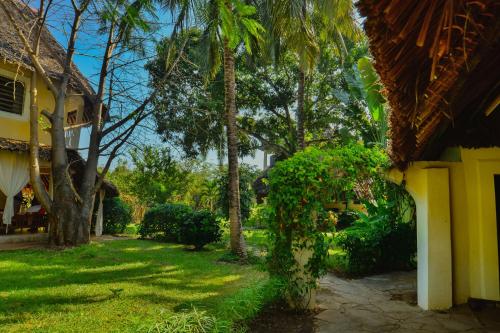 a yard with a yellow house and palm trees at Upani in Diani in Diani Beach