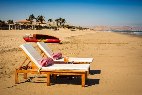 two lounge chairs and a boat on a beach at Vichayito Bungalows & Carpas by Aranwa Hotels in Vichayito