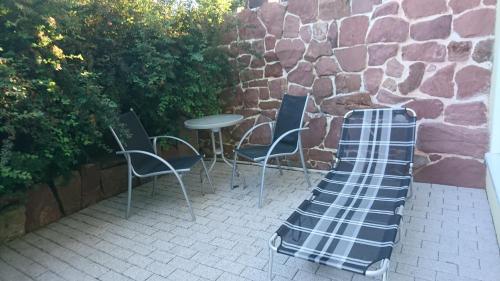 a patio with chairs and a table and a stone wall at Ferienwohnung am Waldchen in Bad Kissingen