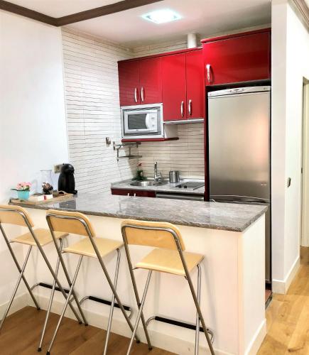 a kitchen with red cabinets and a counter with chairs at CHUECA Apartamentos Noxi in Madrid