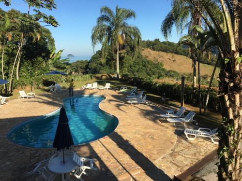 a swimming pool with chairs and an umbrella at Chalé Boiçucanga / Maresias in Boicucanga