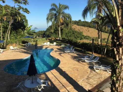 a swimming pool with chairs and an umbrella at Chalé Village do Mirante Boiçucanga in Boicucanga