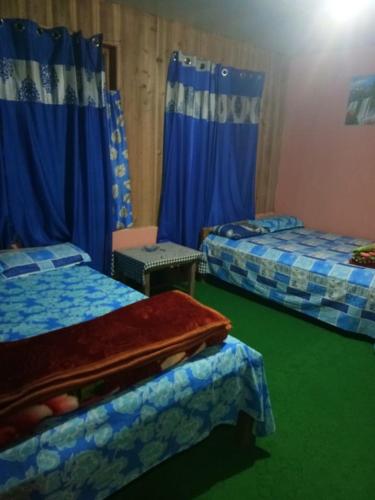 two beds in a room with blue curtains at Vamoose Anugraha in Mangpu