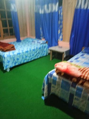 a bedroom with two beds and green floors and blue curtains at Vamoose Anugraha in Mangpu