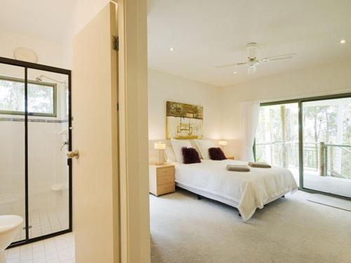 a white bedroom with a bed and a bathroom at Karingal just minutes from Blueys Beach in Charlotte Bay