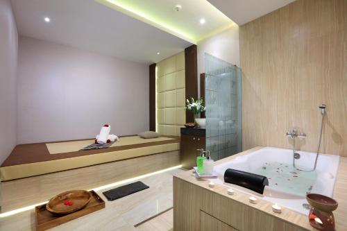 a bathroom with a bath tub and a bed at Harper Palembang by ASTON in Palembang