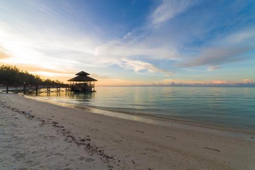 a beach with an umbrella and the ocean at sunset at Sutera at Mantanani Island Resort & Spa in Mantanani Island 