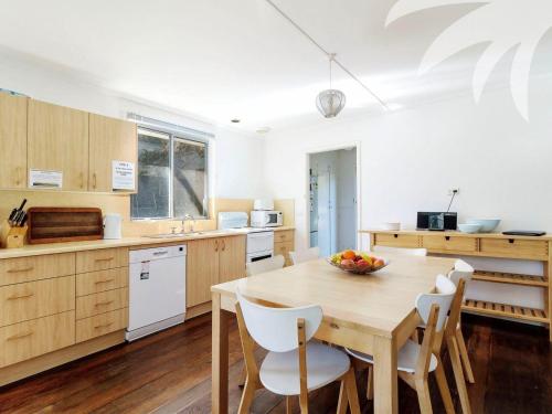 Una cocina con una mesa de madera y sillas blancas. en Pippis a Classic Beach House, en Seal Rocks