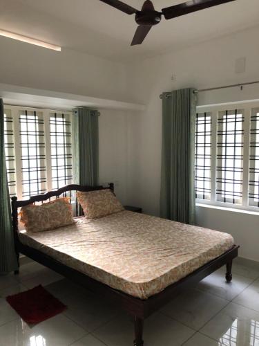 a bedroom with a bed with green curtains and a ceiling fan at Sannidhi Home stay in Guruvāyūr