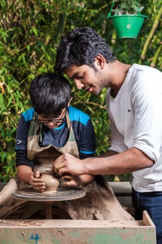 a man teaching a boy how to make a pottery wheel at Rakkh Resort, a member of Radisson Individuals Retreats in Pālampur