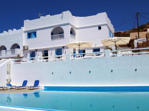 a white building with chairs and umbrellas next to a swimming pool at Hotel Petradi in Ios Chora