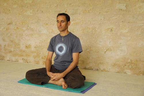 Ein Mann, der in einer Yoga-Pose auf dem Boden sitzt. in der Unterkunft Les Granges de la hulotte, les Mésanges in Lies