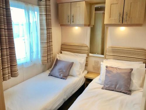 two beds in a small room with a window at Heacham Golden Sunset Caravan Pets go Free in Hunstanton