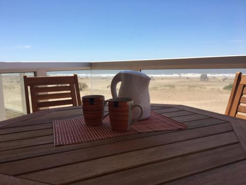 a table with two coffee cups on a table with the beach at Mirasoles 20 in Las Gaviotas