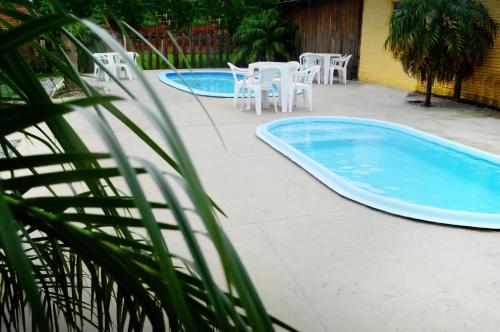two swimming pools with white tables and chairs in a yard at Hotel Glória in São Gabriel