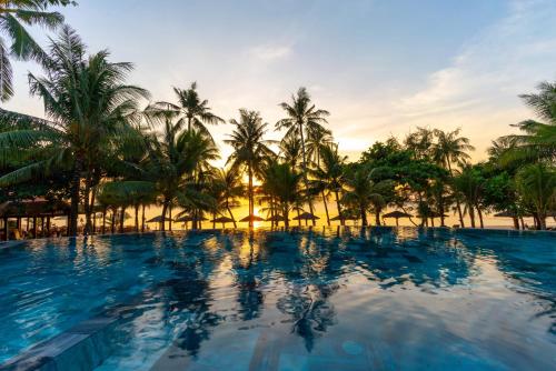 a resort swimming pool with palm trees and a sunset at Thanh Kieu Beach Resort in Phú Quốc