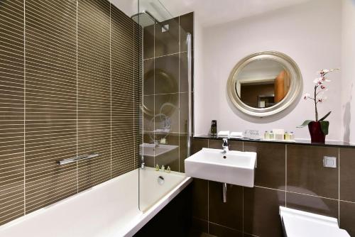 a bathroom with a sink and a tub and a mirror at Fraser Suites Glasgow in Glasgow