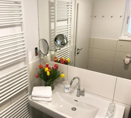 a bathroom with a sink and a mirror and flowers at Art Apart Nomay Summercard Blick Top of Salzburg in Kaprun