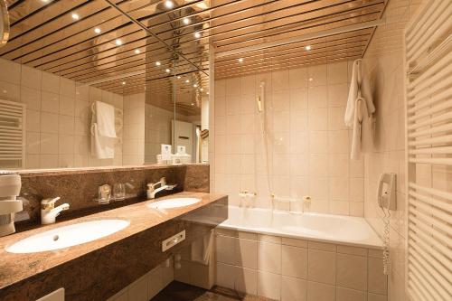 a bathroom with two sinks and a tub and a mirror at Hotel Steffani in St. Moritz