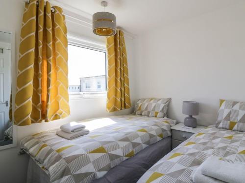 two beds in a bedroom with yellow and grey curtains at Sunbeach Chalets in Great Yarmouth