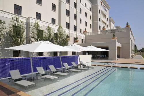 a pool with chairs and umbrellas next to a hotel at Metcourt at Emperors Palace in Kempton Park