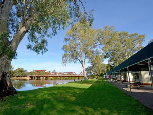 a park with a river and a bridge in the background at Riverbend Caravan Park Renmark in Renmark