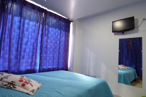 a bedroom with a bed with blue curtains and a television at Hotel La Avenida in Choachí