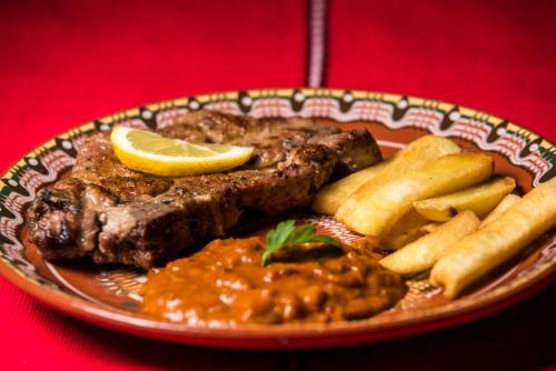 a plate of food with steak and chips and a lemon at Banskovilla Zlateva House in Bansko
