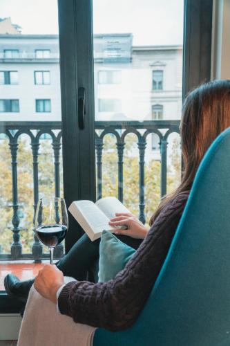 a woman reading a book and a glass of wine at Gran Hotel Havana 4Sup by Escampa Hotels in Barcelona