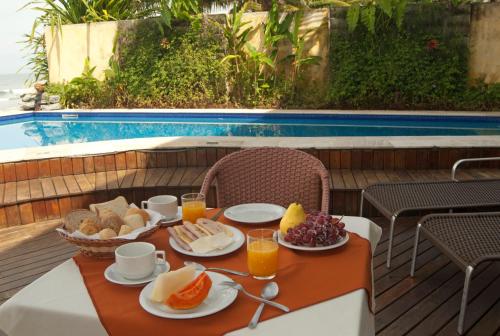 a table with breakfast food and drinks and a pool at Juquehy La Plage Hotel in Juquei