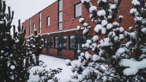 a red brick building with snow covered trees in front of it at Vlantana in Klaipėda