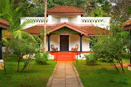 a small white house with a red door and chairs at Mantra Koodam Kumbakonam - a CGH Earth Experience in Kumbakonam