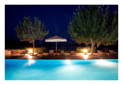 a swimming pool at night with chairs and an umbrella at Alonissos beach villa 5 steps away from the sea in Kalamakia