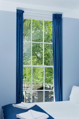 a bedroom with a large window with blue curtains at Angus Hotel in London