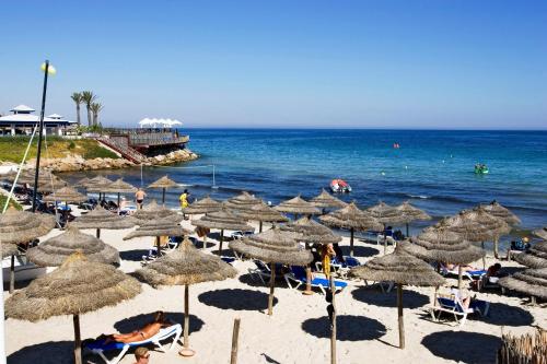 a beach with many straw umbrellas and the ocean at Regency Hotel & Spa in Monastir