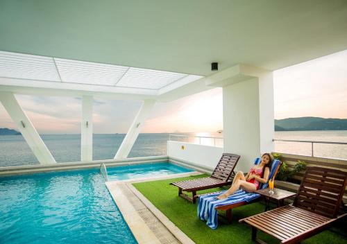 a woman sitting on a chair next to a swimming pool at Dendro beachfront Hotel in Nha Trang