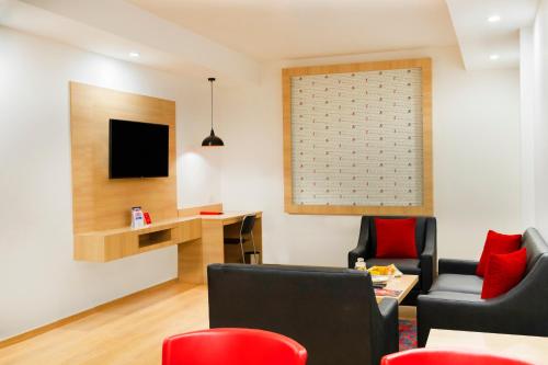 a living room with red chairs and a tv at Red Fox by Lemon Tree Hotels, Dehradun in Dehradun