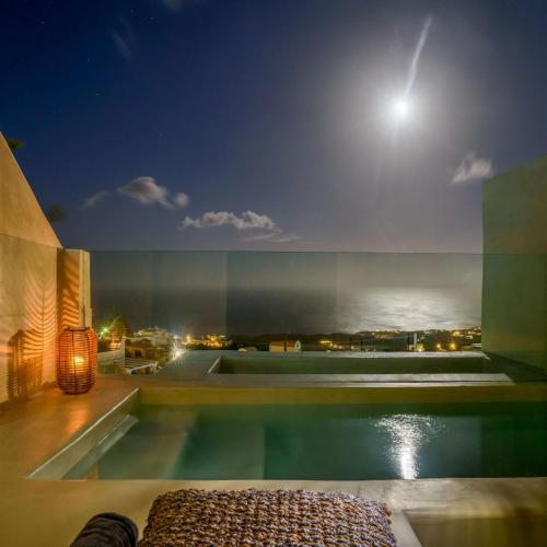 a house with a swimming pool at night with the moon at Divelia East in Imerovigli