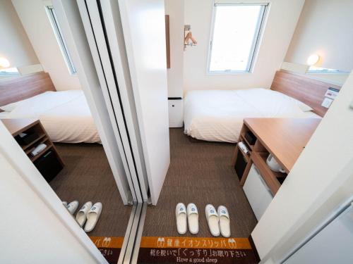 a small room with two beds and a desk with a book at Super Hotel Yamagata Sakurambo-Higashine Station Front in Higashine
