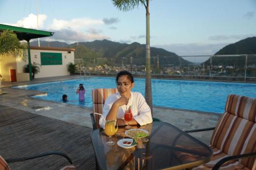a woman sitting at a table next to a pool at Hotel Grand Q Gorontalo in Gorontalo