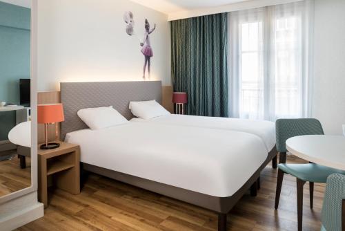 ein Schlafzimmer mit einem großen weißen Bett und einem Tisch in der Unterkunft Aparthotel Adagio Paris Montmartre in Paris