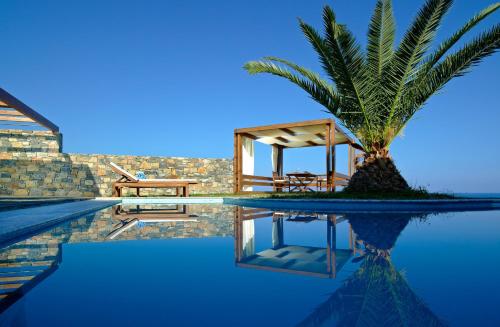 a swimming pool with a palm tree and a house at St. Nicolas Bay Resort Hotel & Villas in Agios Nikolaos
