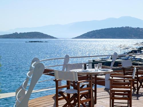 a table and chairs on a deck next to the water at St. Nicolas Bay Resort Hotel & Villas in Agios Nikolaos
